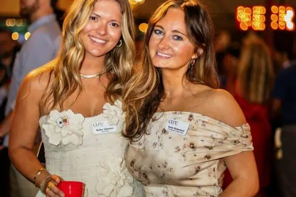 Two smiling women at a charity event holding red cups for CURE Childhood Cancer.