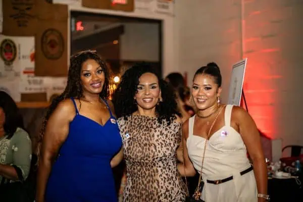 Three women smiling at a CURE Childhood Cancer event in a lively setting.