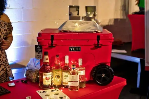 Red YETI cooler with alcohol bottles on table at charity event.