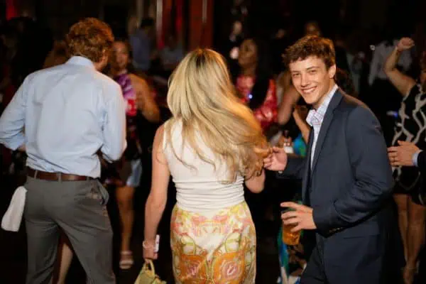 Young man dancing at CURE Childhood Cancer event with diverse crowd.