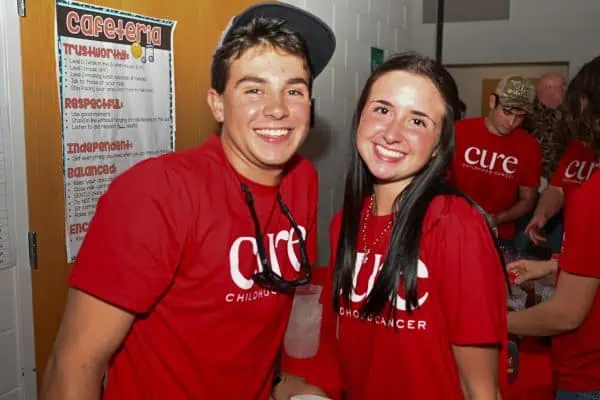 Smiling young man and woman wearing CURE T-shirts at charity event.