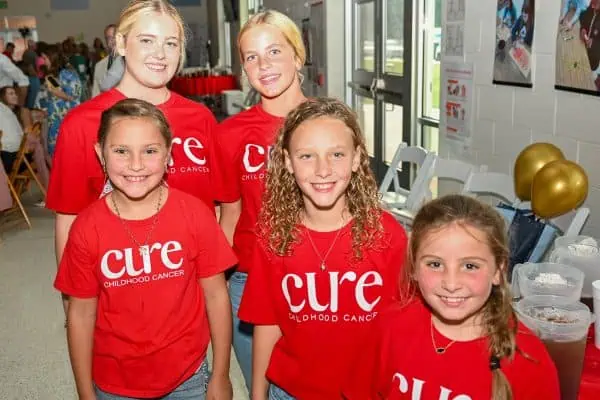 Young volunteers wearing CURE Childhood Cancer T-shirts at a charity event.