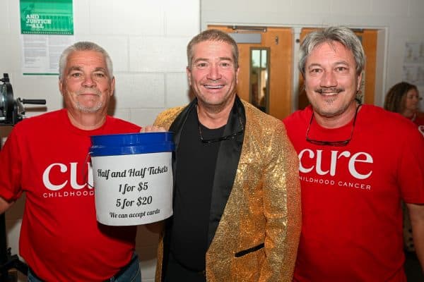 Three men at CURE Childhood Cancer event, one holding donation bucket.