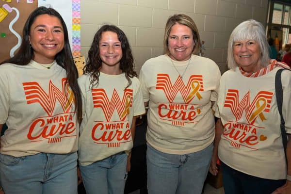 Group of women wearing CURE Childhood Cancer T-shirts at event.
