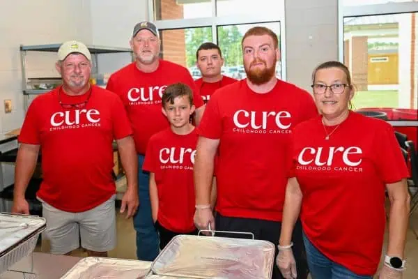 Group of volunteers wearing CURE Childhood Cancer shirts at event.