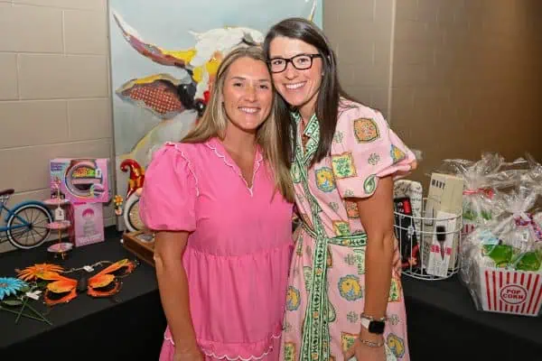 Two women smiling at CURE Childhood Cancer event with gifts and decorations.
