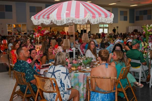 People enjoying a charity event under a pink and white striped umbrella.