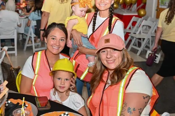 Women and children at CURE Childhood Cancer event wearing safety vests and helmets.