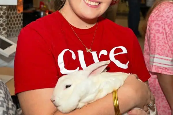 Young girl holding a white rabbit at CURE Childhood Cancer event.