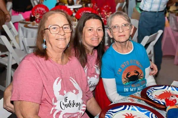 Three women smiling at a CURE Childhood Cancer event with lobster-themed shirts.