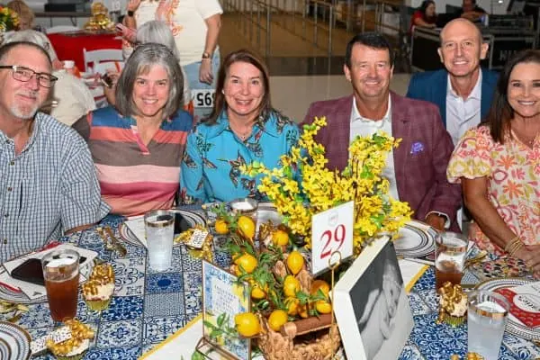 Group of people celebrating at CURE Childhood Cancer event with floral centerpiece.