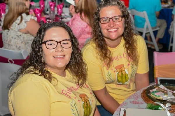 Two smiling women at CURE Childhood Cancer event wearing yellow shirts.